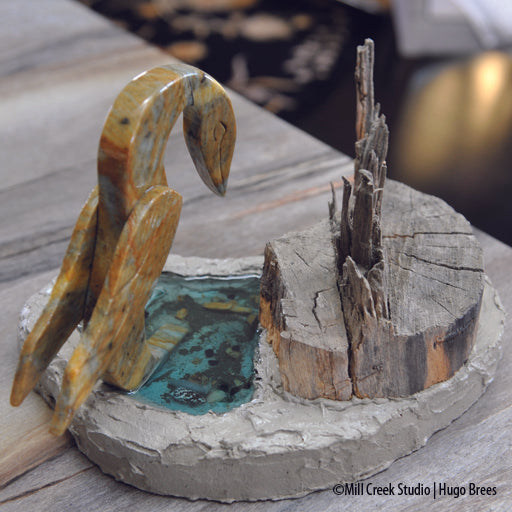 This mixed media soapstone piece depicts a bird fishing in it's environment of tree, water, and mollusks.
