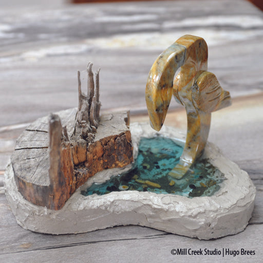 This mixed media soapstone piece depicts a bird fishing in it's environment of tree, water, and mollusks.